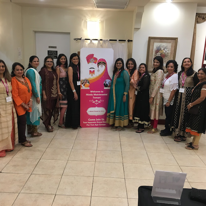 Women volunteers posing beside the Hindu Matrimonial Tampa welcome banner